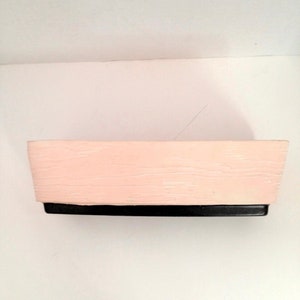 May include: A rectangular planter with a light pink finish and a black base. The planter has a wood-grain texture.