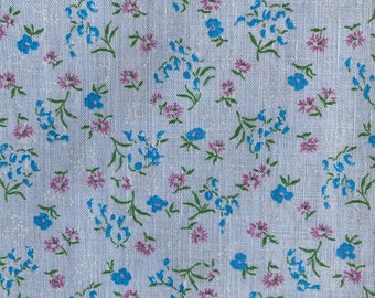 May include: White fabric with a repeating pattern of small blue and pink flowers. The flowers are scattered randomly across the fabric.