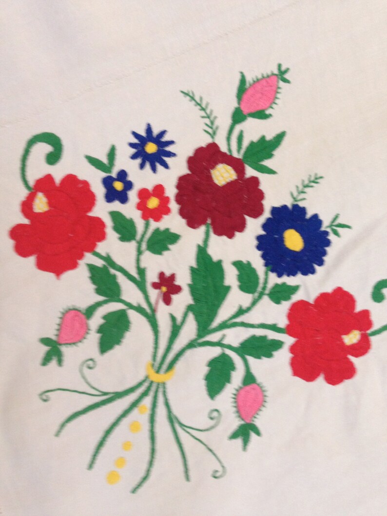 K&ouml;nnte beinhalten: Gestickte Blumenmuster auf wei&szlig;em Stoff mit roten, rosa, blauen, gelben und gr&uuml;nen Blumen. Das Design umfasst eine Vielzahl von Blumenformen und -gr&ouml;&szlig;en und schafft ein optisch ansprechendes und komplexes Muster.