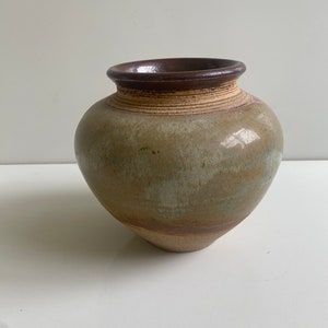 May include: A brown and green ceramic vase with a rounded body and a slightly flared rim. The vase has a speckled glaze with brown and green accents.