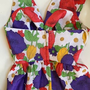 May include: A sleeveless dress with a floral pattern featuring red, purple, and yellow flowers on a white background. The dress has a V-neckline and a gathered waist. The fabric appears to be cotton or a similar lightweight material.
