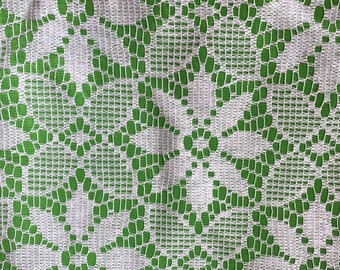 May include: White lace fabric with a green background. The lace has a floral pattern.