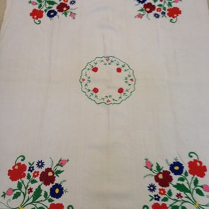 K&ouml;nnte beinhalten: Wei&szlig;e Tischdecke mit gestickten Blumendesigns in Rot, Gr&uuml;n, Blau und Rosa. Die Tischdecke hat ein kreisf&ouml;rmiges Design in der Mitte.