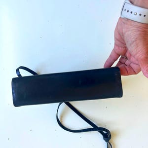 Pode incluir: Uma bolsa retangular preta com uma al&ccedil;a fina. A bolsa &eacute; feita de um material brilhante e tem um design simples e elegante. A al&ccedil;a &eacute; em la&ccedil;o e amarrada na extremidade.