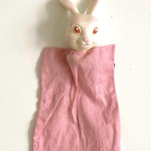 May include: A vintage bunny hand puppet. The bunny head is white with pink accents on the ears and nose, and orange eyes. The puppet's body is made of pink fabric.