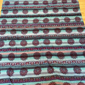 May include: A teal and burgundy striped fabric with a repeating pattern of stylized floral medallions. The fabric has a fringed edge.