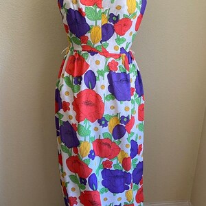 May include: A vintage halter-neck maxi dress with a vibrant floral pattern. The dress features large red and purple flowers with green leaves on a white background. The dress is displayed on a dress form.