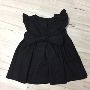 May include: A black sleeveless dress with a bow in the back and ruffled sleeves.