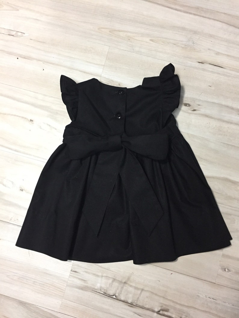 May include: A black sleeveless dress with a bow in the back and ruffled sleeves.
