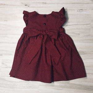 May include: A red and white gingham dress with a bow at the back. The dress has a sleeveless design and a ruffled neckline.
