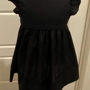 May include: A black sleeveless dress with a ruffled neckline and a gathered skirt. The dress is on a white mannequin.