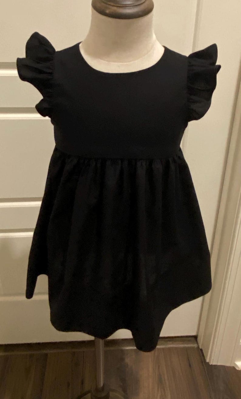 May include: A black sleeveless dress with a ruffled neckline and a gathered skirt. The dress is on a white mannequin.