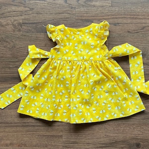May include: A yellow sleeveless dress with a bee print and a matching yellow sash. The dress has a gathered skirt and a ruffled neckline.