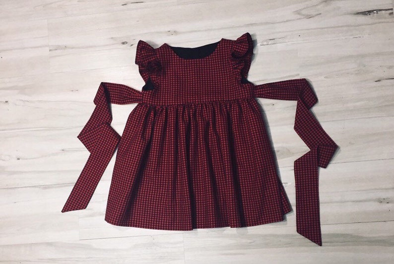 May include: A red and black gingham dress with a black bodice and ruffled sleeves. The dress has a tie at the waist and is sleeveless.