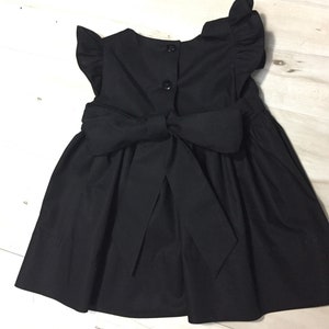 May include: A black sleeveless dress with a large bow in the back and ruffle sleeves.