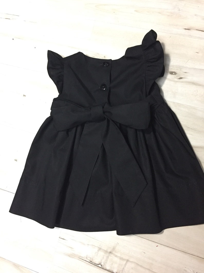 May include: A black sleeveless dress with a large bow in the back and ruffle sleeves.