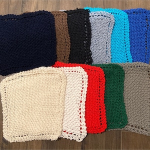 May include: A collection of 12 knitted dishcloths in various colors, including navy blue, brown, black, gray, turquoise, blue, cream, white, red, green, and gray. The dishcloths are all square and have a crocheted border.