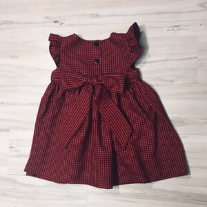 May include: A red and black gingham dress with a bow at the waist and ruffle sleeves.