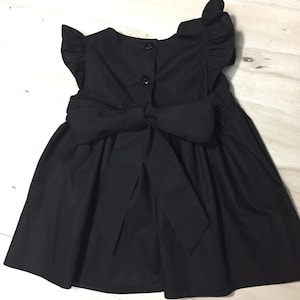 May include: A black sleeveless dress with a bow in the back and ruffle sleeves.