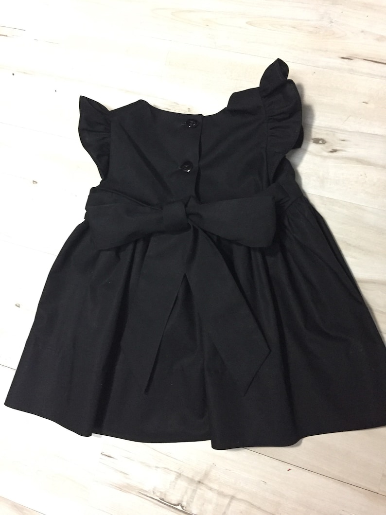 May include: A black sleeveless dress with a bow in the back and ruffle sleeves.