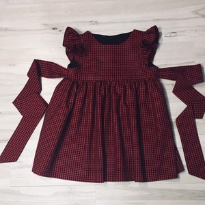 May include: A red and black gingham dress with a ruffled neckline and a bow tie at the waist.