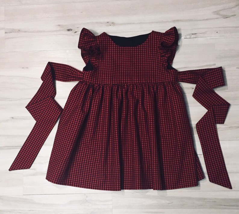 May include: A red and black gingham dress with a ruffled neckline and a bow tie at the waist.