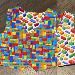 May include: A colorful vest with a Lego block pattern. The vest is made of fabric and has a button closure.