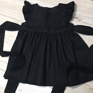 May include: A black sleeveless dress with a ruffled neckline and a large bow at the back.