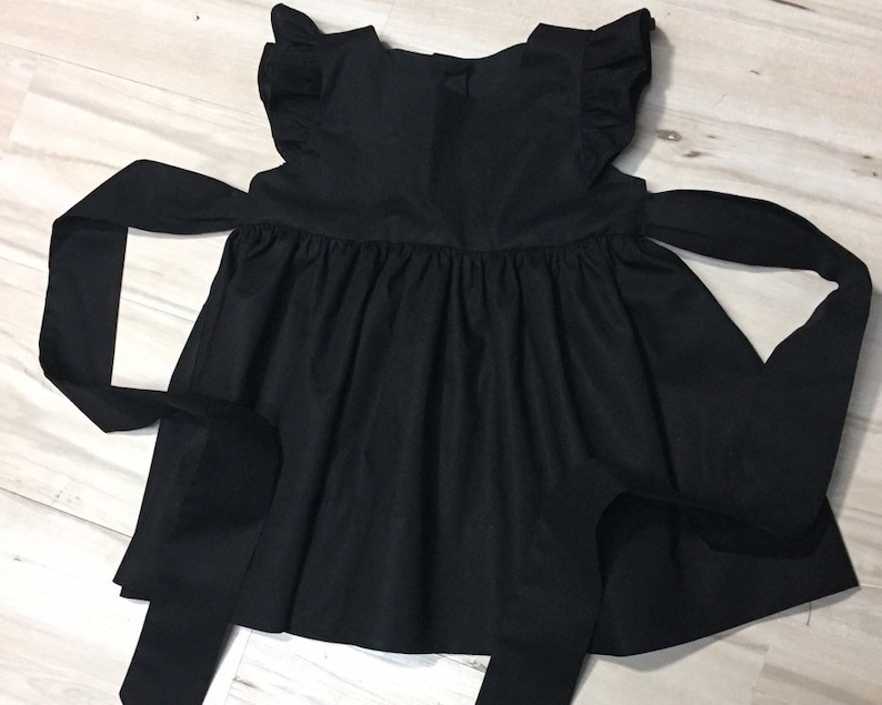 May include: A black sleeveless dress with a ruffled neckline and a large bow at the back.