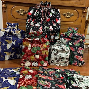 May include: A collection of Christmas-themed drawstring gift bags in various sizes and patterns. Designs include gnomes, ornaments, pine cones, and vintage trucks. The bags are made of fabric and tied with coordinating drawstrings, perfect for holiday gifting.