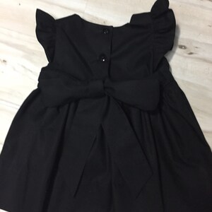 May include: A black sleeveless dress with a bow in the back and ruffled sleeves.