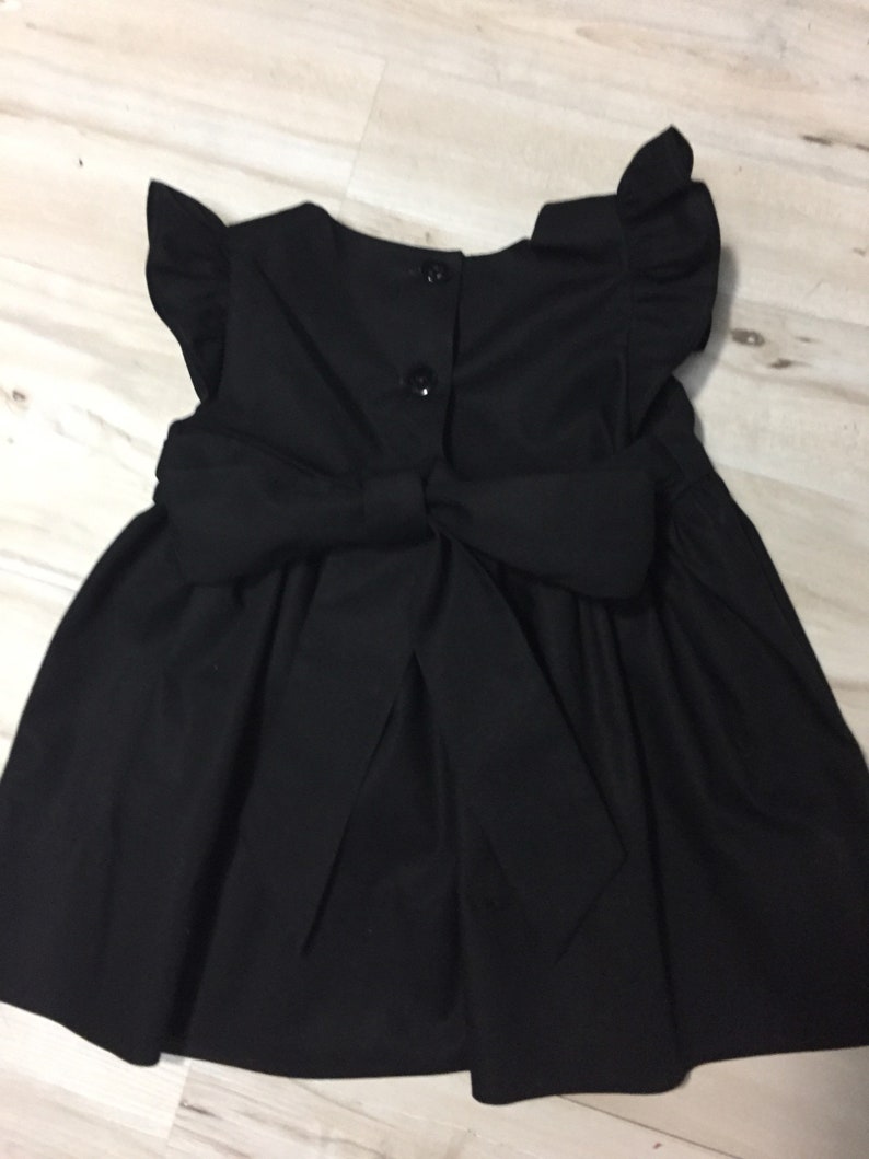 May include: A black sleeveless dress with a bow in the back and ruffled sleeves.