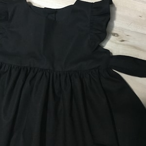 May include: A black sleeveless dress with a ruffled neckline and a bow tie at the waist.