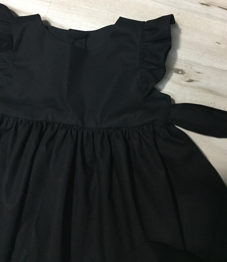 May include: A black sleeveless dress with a ruffled neckline and a bow tie at the waist.