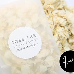 Puede incluir: Una bolsa de organza blanca llena de p&eacute;talos de flores de color marfil. La bolsa tiene una pegatina redonda blanca con el texto "Toss the Petals & Shout Hooray".