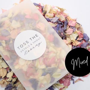 Puede incluir: Una bolsa de pl&aacute;stico transparente llena de una mezcla de p&eacute;talos de flores secas en tonos de rosa, blanco y morado. La bolsa tiene una pegatina circular blanca con el texto "Toss the Petals & Shout Hooray". Una pegatina circular negra con el texto "Mixed" est&aacute; en la mesa junto a la bolsa.