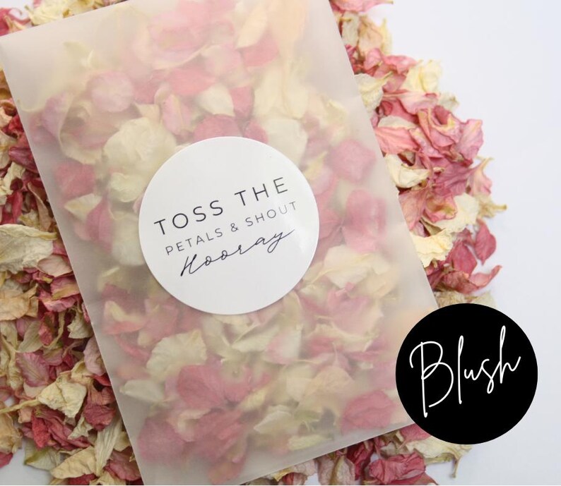 Puede incluir: Una bolsa de pl&aacute;stico transparente llena de p&eacute;talos de flores rosas y blancas. La bolsa tiene una pegatina circular blanca con el texto "Toss the petals & shout Hooray". Una pegatina circular negra con el texto "Blush" est&aacute; en la esquina inferior derecha.