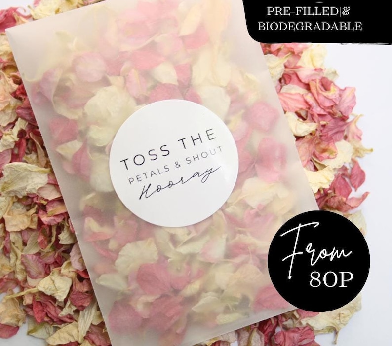 Puede incluir: Una bolsa de pl&aacute;stico transparente llena de p&eacute;talos de rosa rosa y blancos. La bolsa tiene una pegatina circular blanca con el texto "Toss the petals & shout Hooray" y una pegatina circular negra con el texto "From 80p". La bolsa est&aacute; etiquetada como "Pre-filled & Biodegradable".