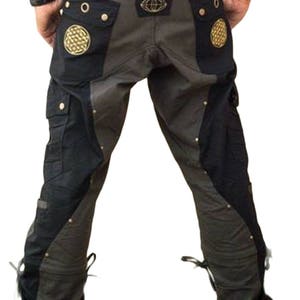 May include: Black and gray cargo pants with decorative stitching and metal accents. The pants have a unique design with a black panel on the front and back, and a gray panel on the sides. The pants have multiple pockets and a drawstring at the bottom of each leg.
