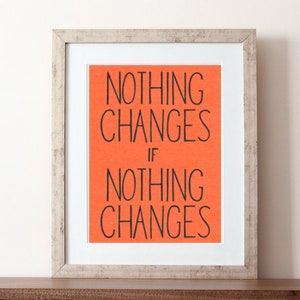 May include: A framed print with a motivational quote on a bright orange background. The quote reads "Nothing changes if nothing changes."