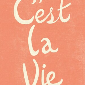 May include: A peach-colored background with the French phrase "C'est la vie" written in white cursive script.