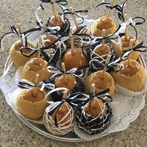 Op de afbeelding: Een schaal met karamel appels versierd met witte en zwarte chocolade gedruppelde ontwerpen en graham cracker kruimels.