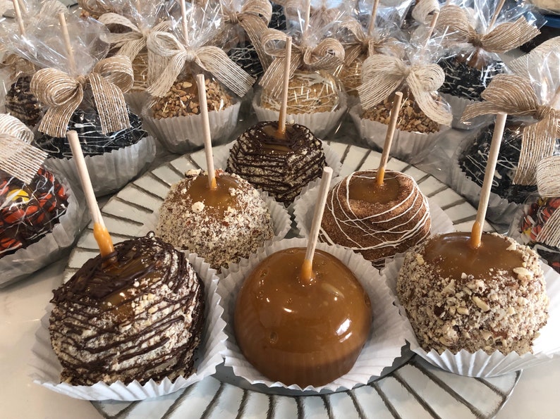 Op de afbeelding: Een schaal met karamel appels versierd met verschillende toppings, waaronder chocolade, noten en witte chocolade drizzle. De appels zijn gerangschikt op een witte en zilveren schaal.