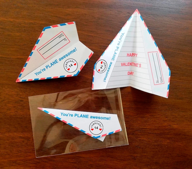 Może przedstawiać: Trzy papierowe karty w kształcie samolotu z tekstem "You're PLANE awesome!" i sercem z tekstem "February 14" na każdej. Środkowa karta ma tekst "Happy Valentine's Day" i puste miejsce na imię.