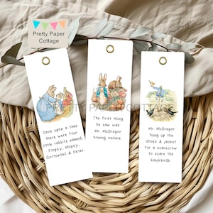 Puede incluir: Tres marcapáginas blancos con ilustraciones y texto de un cuento infantil. Los marcapáginas presentan imágenes de conejos, un espantapájaros y texto, incluyendo "Érase una vez" y "Sr. McGregor". Cada marcapáginas tiene un ojal dorado.