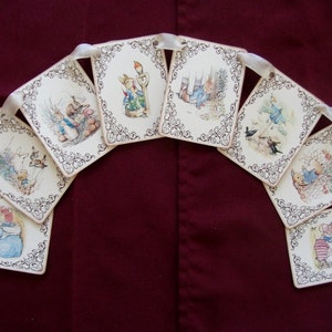 May include: A garland of square cards featuring illustrations of rabbits in various scenes. Each card has a decorative border and is connected by a white ribbon. The background is a deep burgundy color.