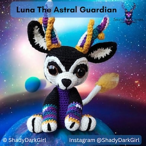 Könnte beinhalten: Ein gehäkeltes Plüschtier in Form eines Rehs mit einem schwarz-weißen Körper, lila und gelben Geweih und großen, runden Augen. Das Spielzeug sitzt auf einer blauen und weißen, planetartigen Oberfläche. Der Text "Luna The Astral Guardian" befindet sich oben im Bild. Der Text "ShadyDarkCharms" befindet sich in der oberen rechten Ecke des Bildes. Der Text "ShadyDarkGirl" befindet sich in der unteren linken Ecke des Bildes. Der Text "Instagram @ShadyDarkGirl" befindet sich in der unteren rechten Ecke des Bildes.