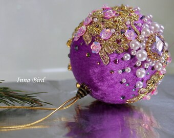 May include: Purple velvet Christmas bauble decorated with gold trim, pink sequins, and white pearls.