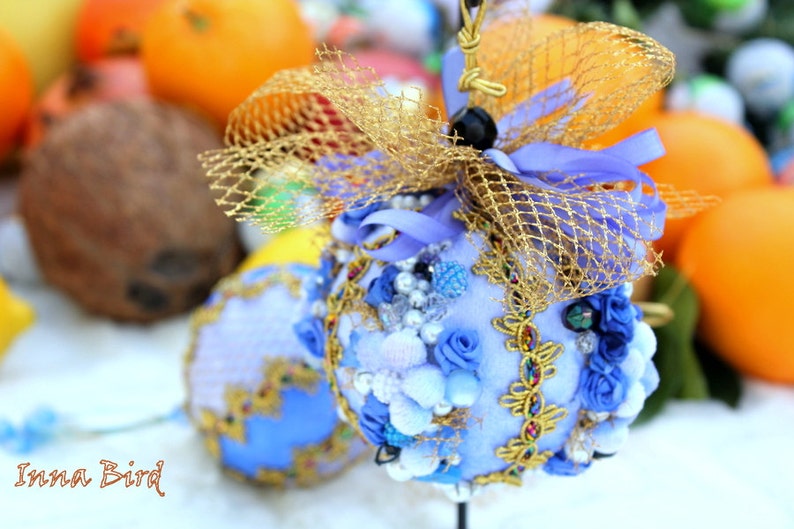 May include: A blue and gold decorative ornament with a net-like design and pearl-like accents. The ornament is decorated with blue and white flowers and is sitting on a white surface.
