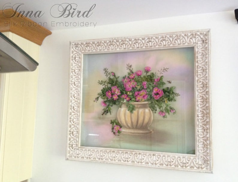May include: A white framed picture featuring a pink and green floral arrangement in a beige pot. The picture is titled "Inna Bird Silk Ribbon Embroidery".